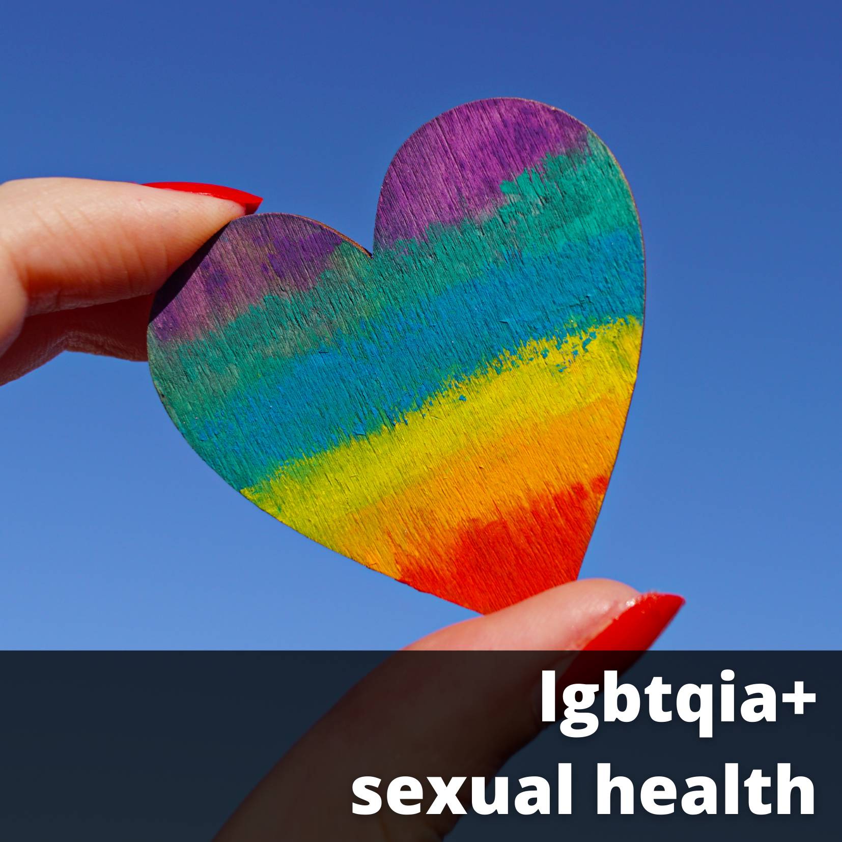 Fingers holding a wooden heart with rainbow colors in front of a blue sky